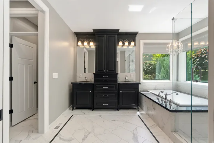 Bathroom featuring dual black vanities with integrated storage, marble-patterned floor tiling with a dark border, a built-in soaking tub, and a clear glass shower enclosure