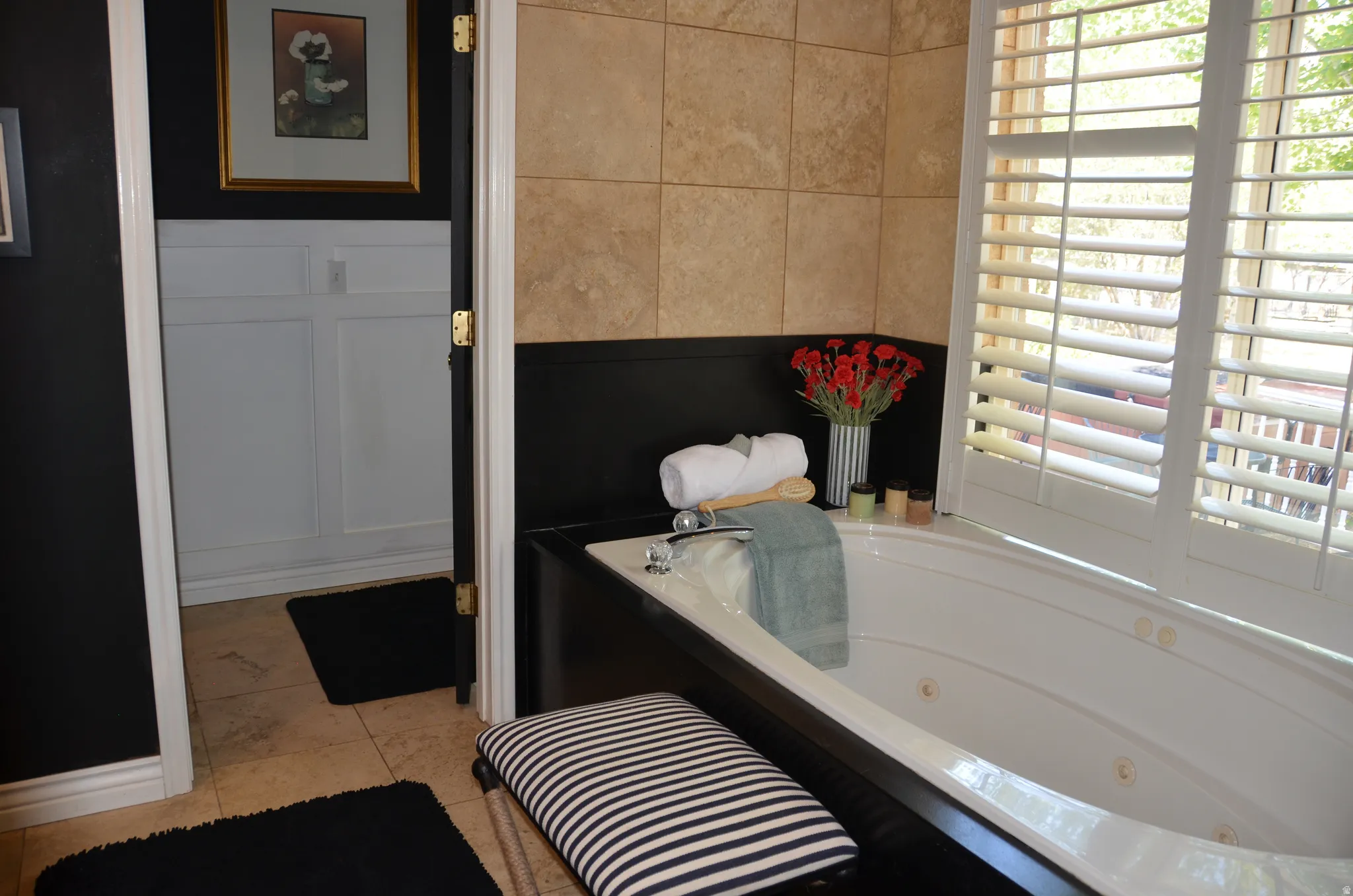 Master Bathroom: Soaking tub featuring a tiled surround, black wainscoting, and white plantation shutters