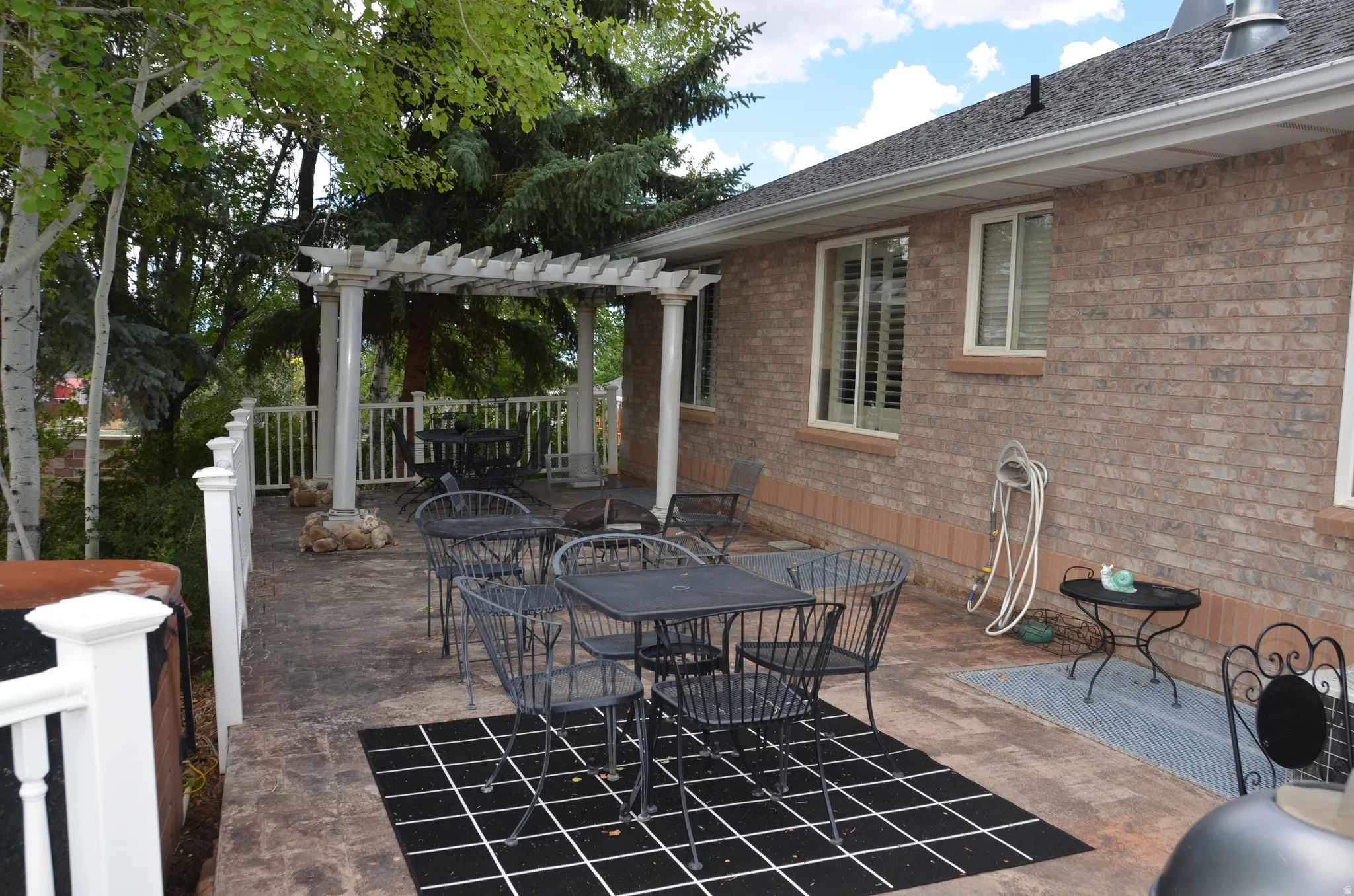 Extensive stamped concrete patio featuring a white pergola, white railing, and a brick exterior facade