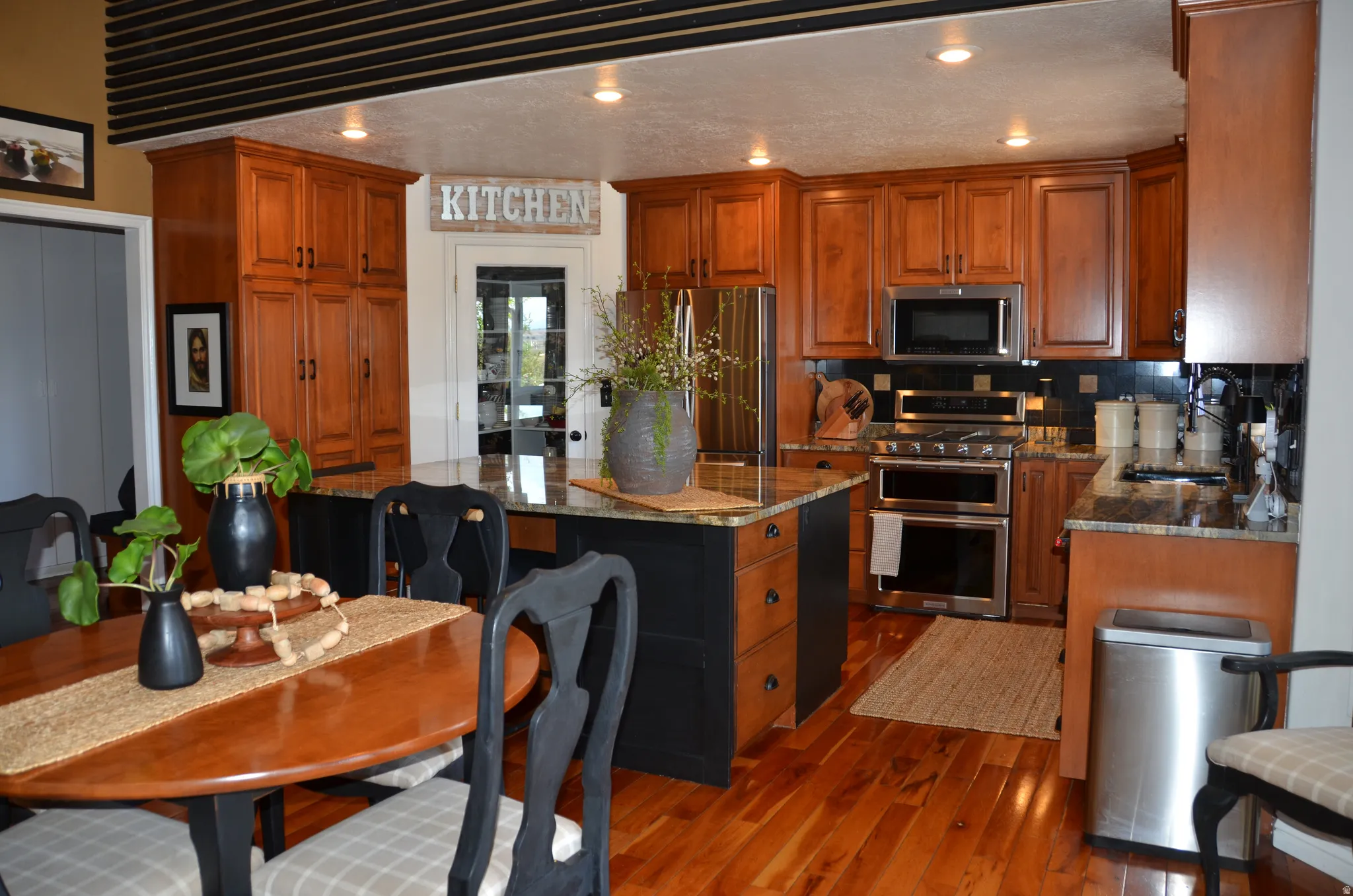 Kitchen featuring warm wood cabinetry, stainless steel appliances, a center island with countertop seating, a tiled backsplash, and wood flooring