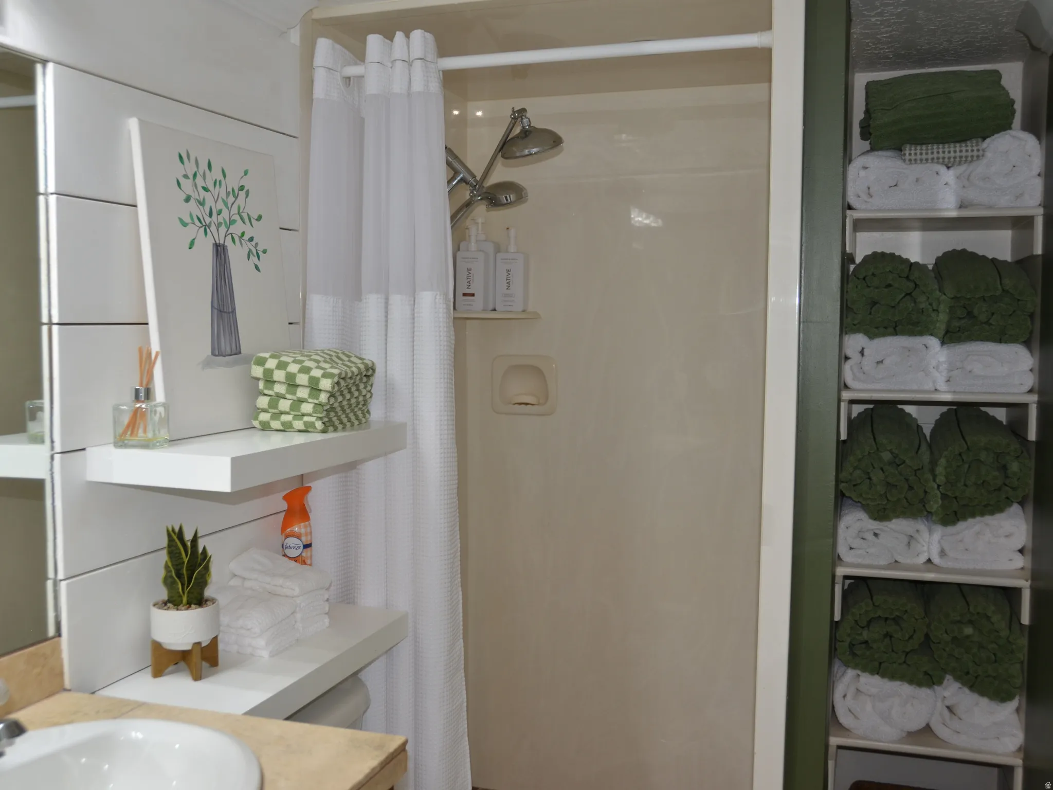 Bathroom featuring a shower stall with built-in shelving, white floating shelves, and a vanity with an integrated sink