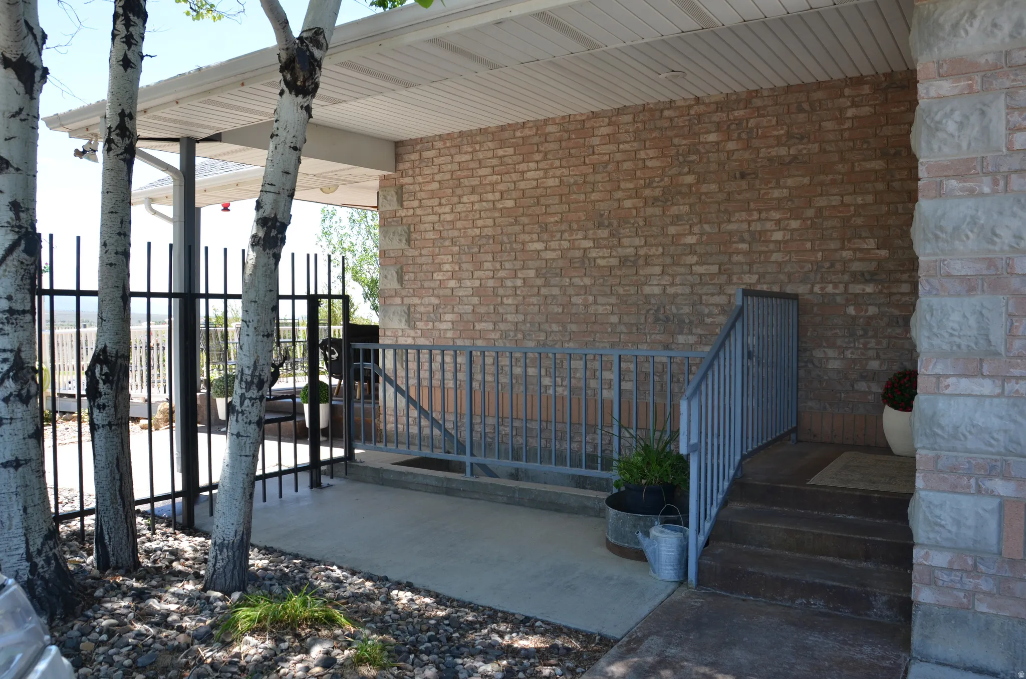 Exterior doors - walk out basement and upstairs into laundry/mudroom.  Covered patio area featuring a brick and stone exterior, concrete flooring, and metal railings