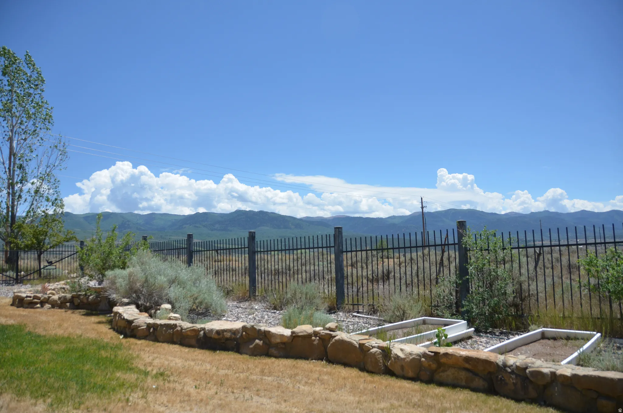 Landscaped yard featuring a stone retaining wall, raised garden beds, and a black wrought iron fence