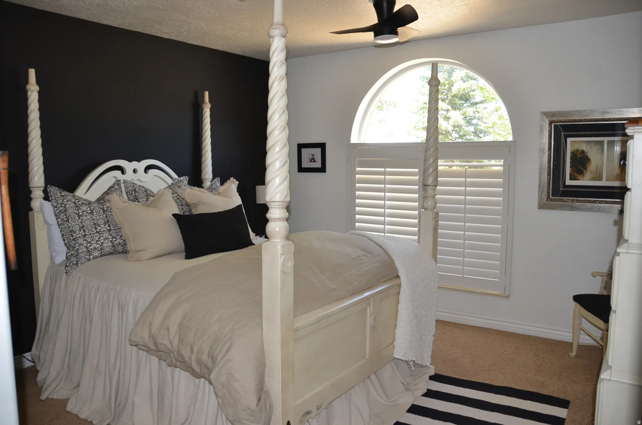 Arched window with plantation shutters, complimented by neutral carpeting and a ceiling fan