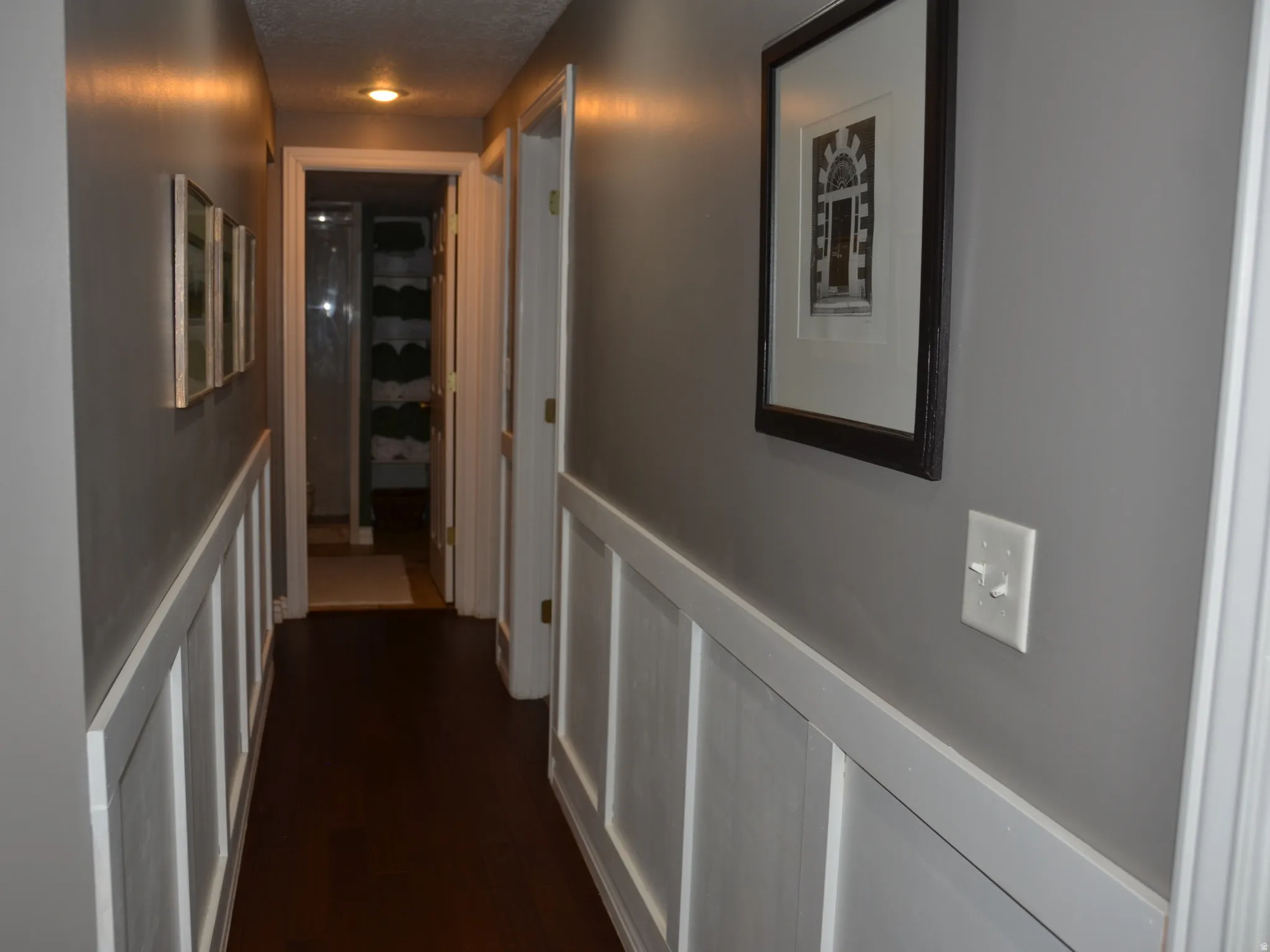 Hallway featuring dark wood-finish flooring, white wainscoting, light gray walls, recessed lighting, and white trim around doorways