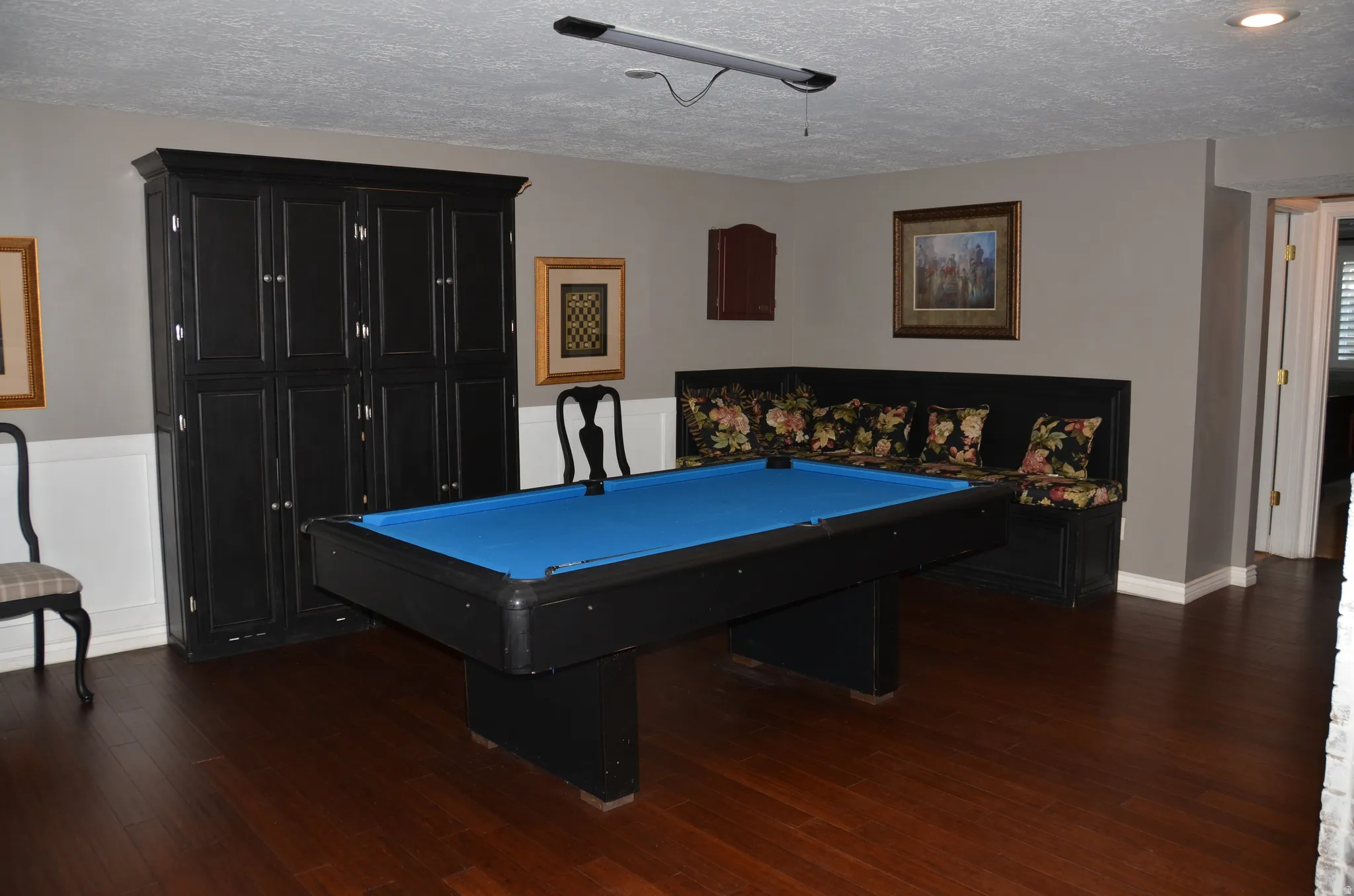 Game room featuring wood-finish flooring, wainscoting, built-in storage cabinetry, and built-in corner seating
