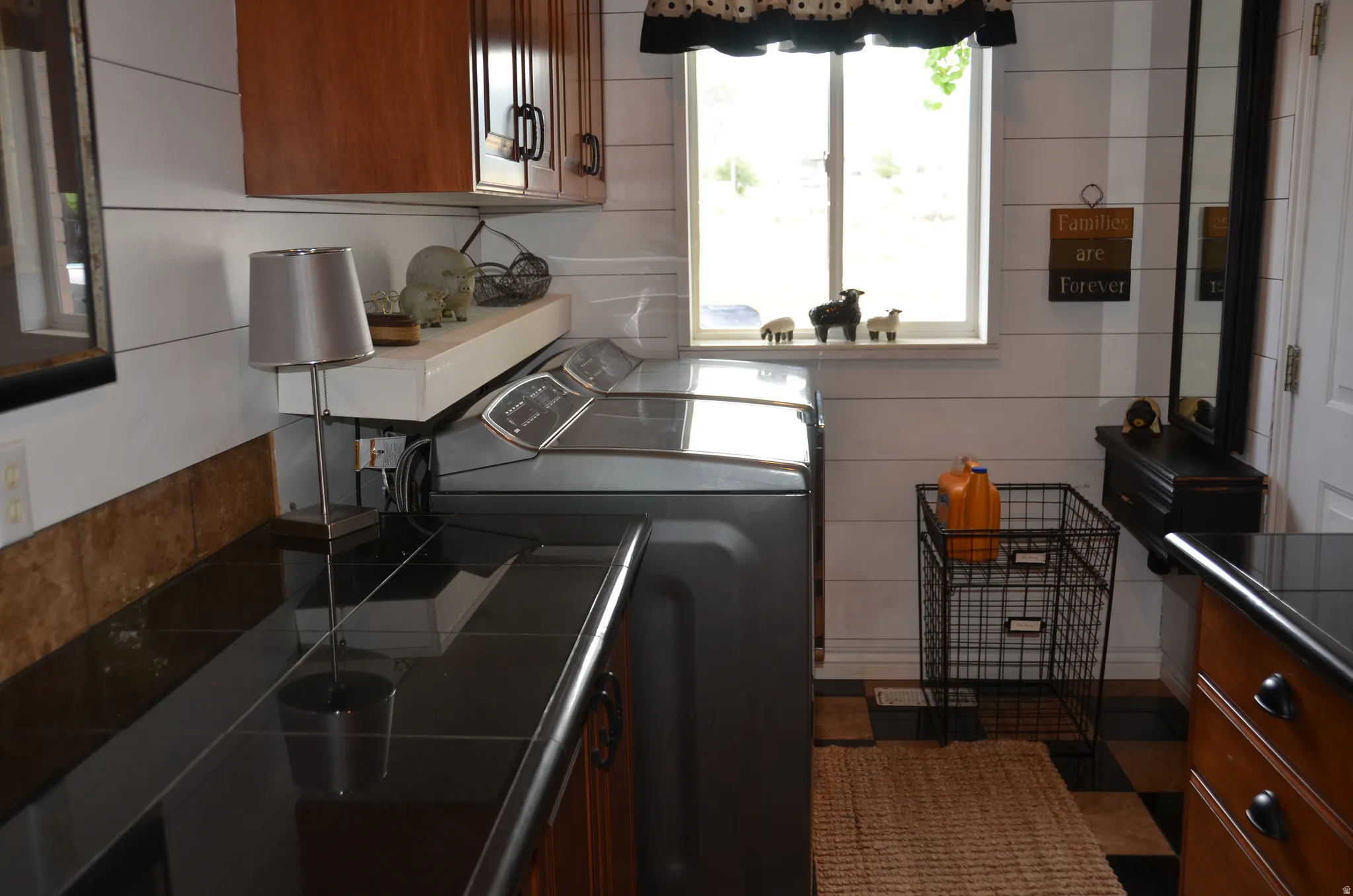 Laundry area featuring wood-finish cabinetry, black tile countertops, and shiplap wall paneling
