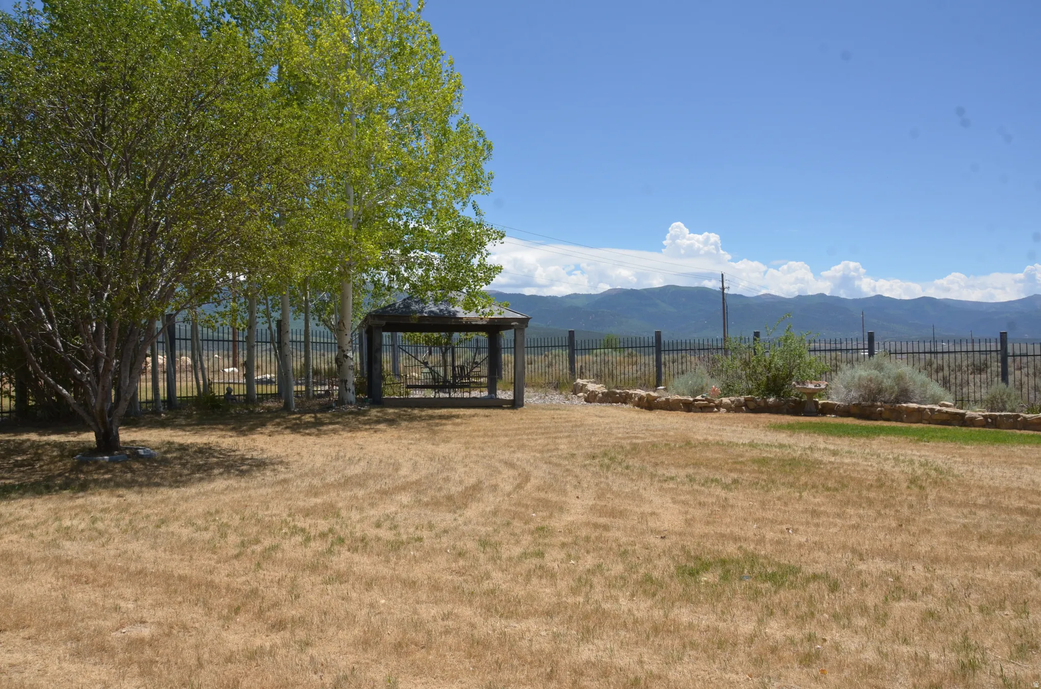 Expansive outdoor space featuring a metal gazebo, mature trees, and a black wrought iron fence