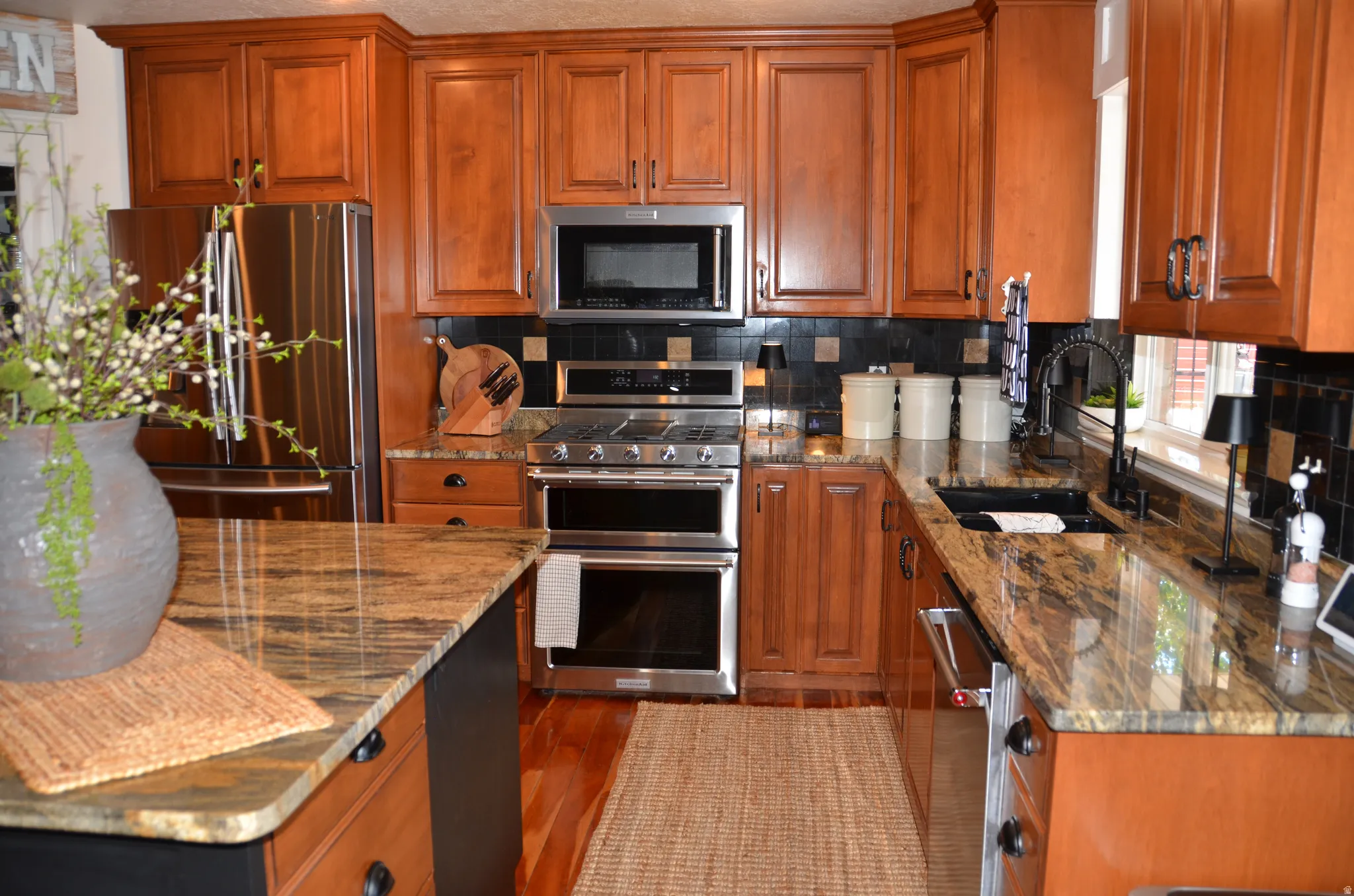 Kitchen featuring abundant wood cabinetry, stainless steel appliances including a double oven and refrigerator, stone countertops, and a tile backsplash