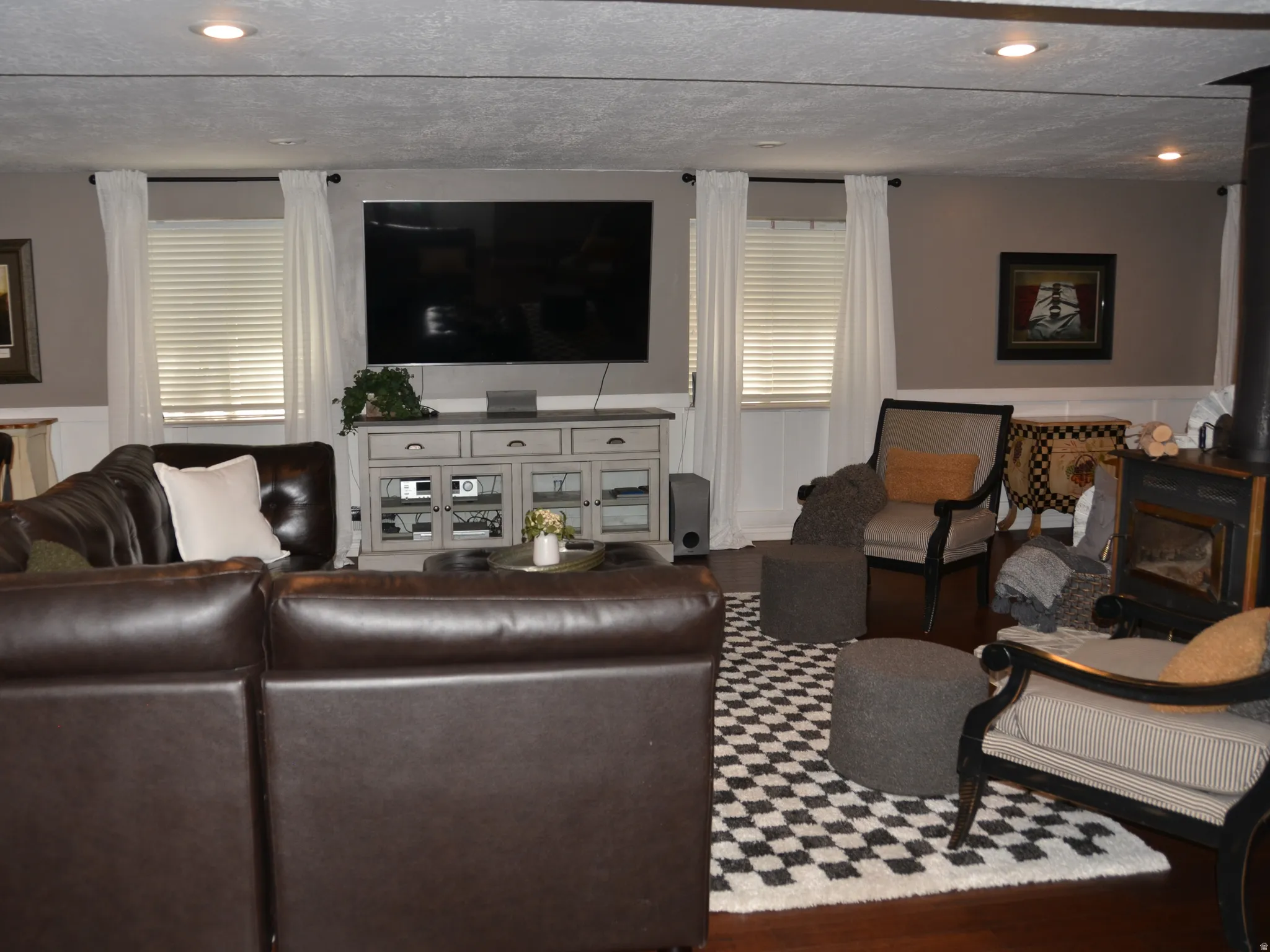 Spacious living area featuring wood-finish flooring, recessed lighting, white wainscoting, and a prominent wood stove