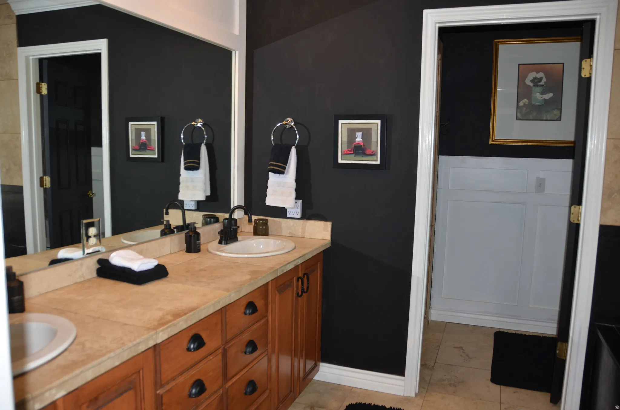 Master Bathroom vanity featuring dual sinks with black fixtures, a stone-finish countertop, and wood cabinetry with dark hardware
