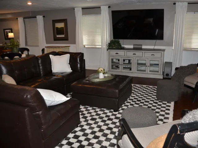 Spacious living area featuring dark wood-finish flooring, white window treatments.