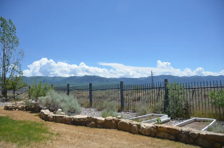 Landscaped yard featuring a stone retaining wall, raised garden beds, and a black wrought iron fence