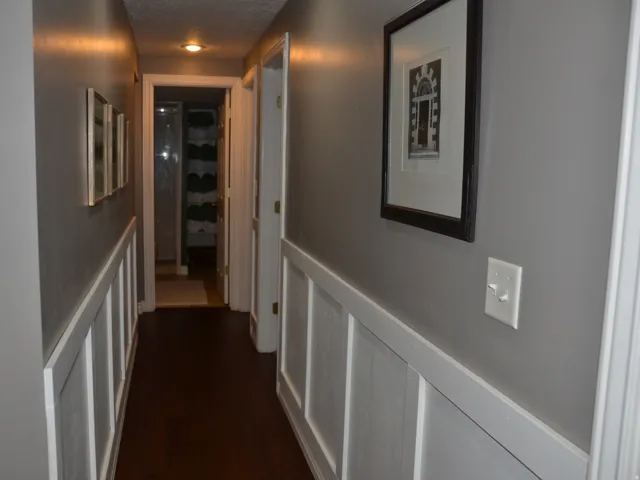 Hallway featuring dark wood-finish flooring, white wainscoting, light gray walls, recessed lighting, and white trim around doorways