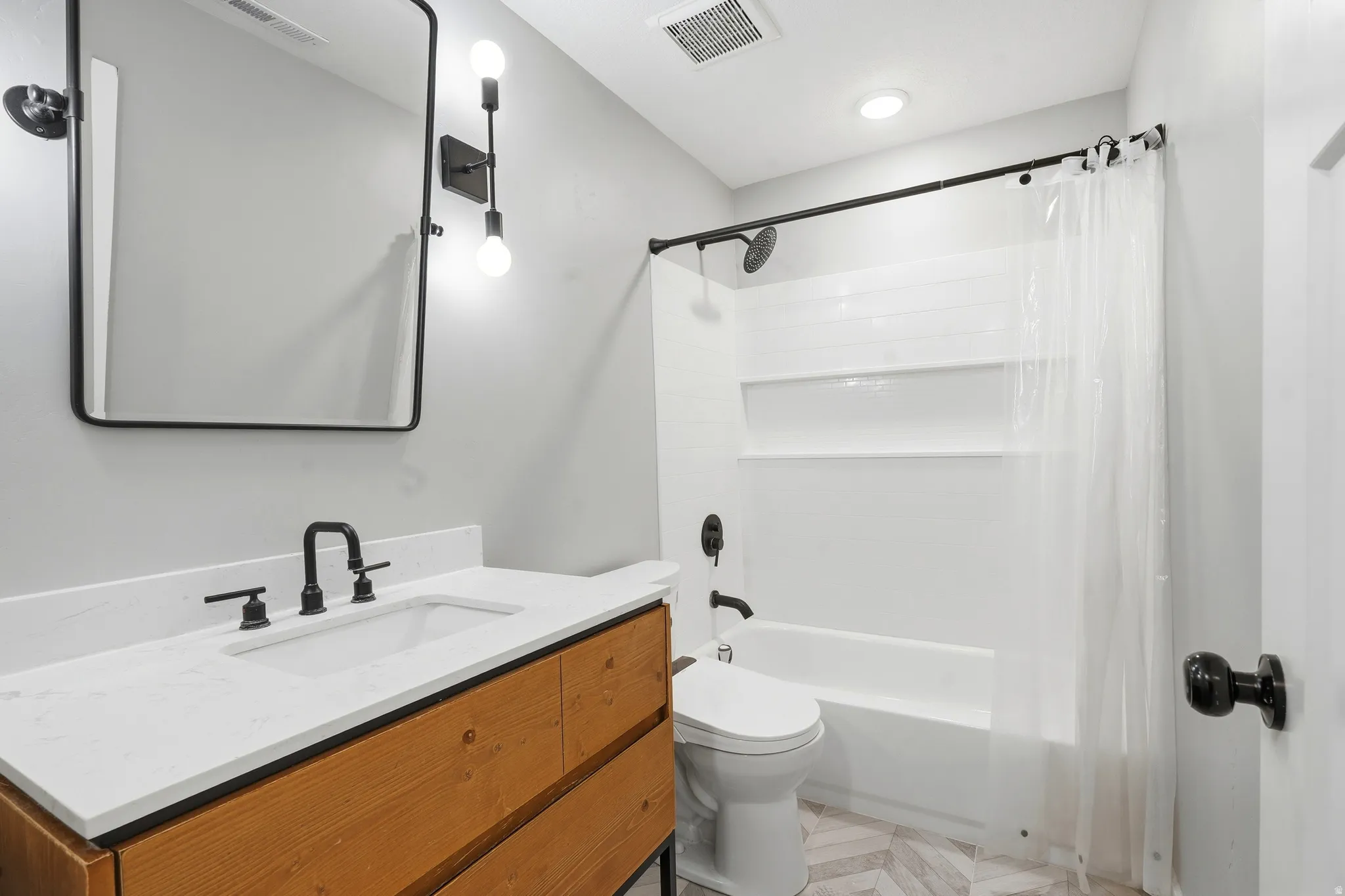 Bathroom featuring a wood-finish vanity with a white countertop and integrated sink, matte black faucet, and a rectangular mirror with a black frame