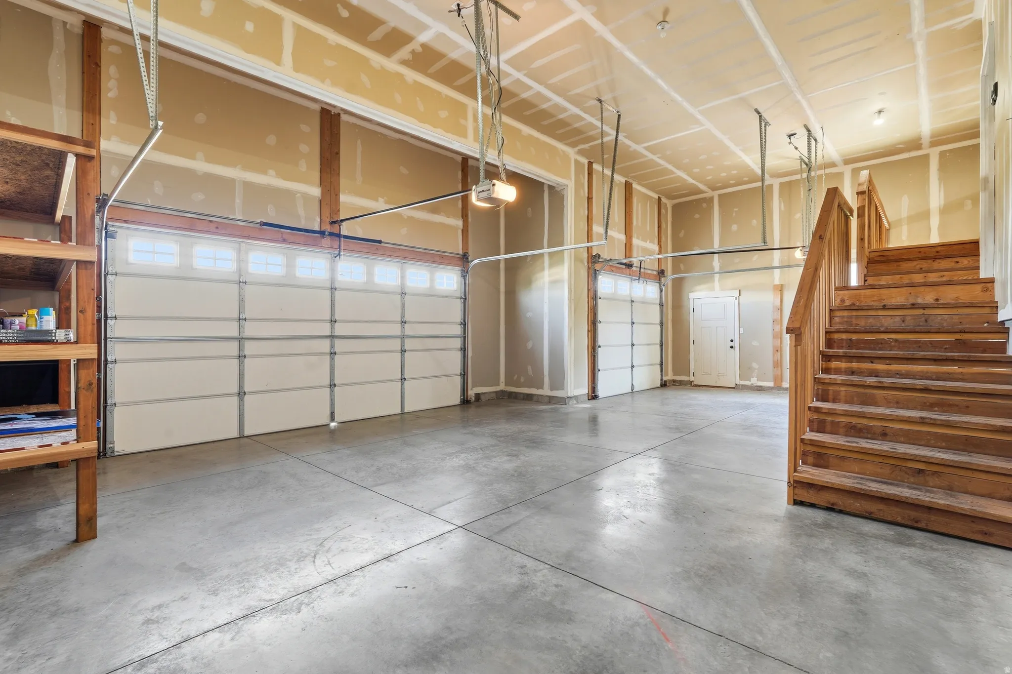 Spacious garage featuring two overhead doors with window panels, concrete flooring, and an exposed wood staircase