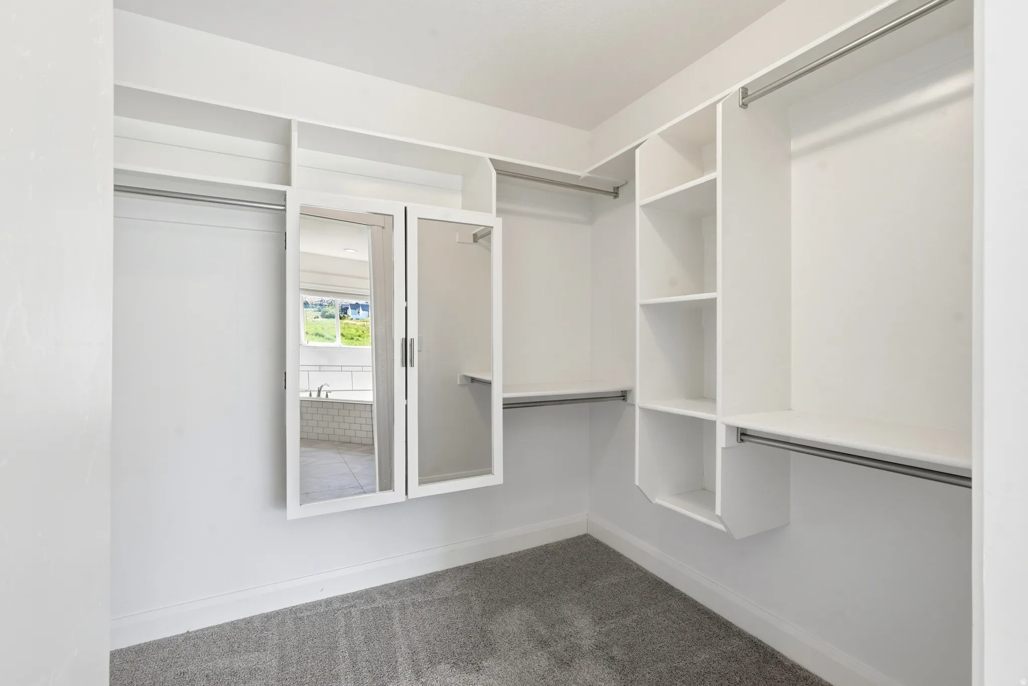 Walk-in closet featuring white built-in shelving, multiple hanging rods, and a mirrored cabinet