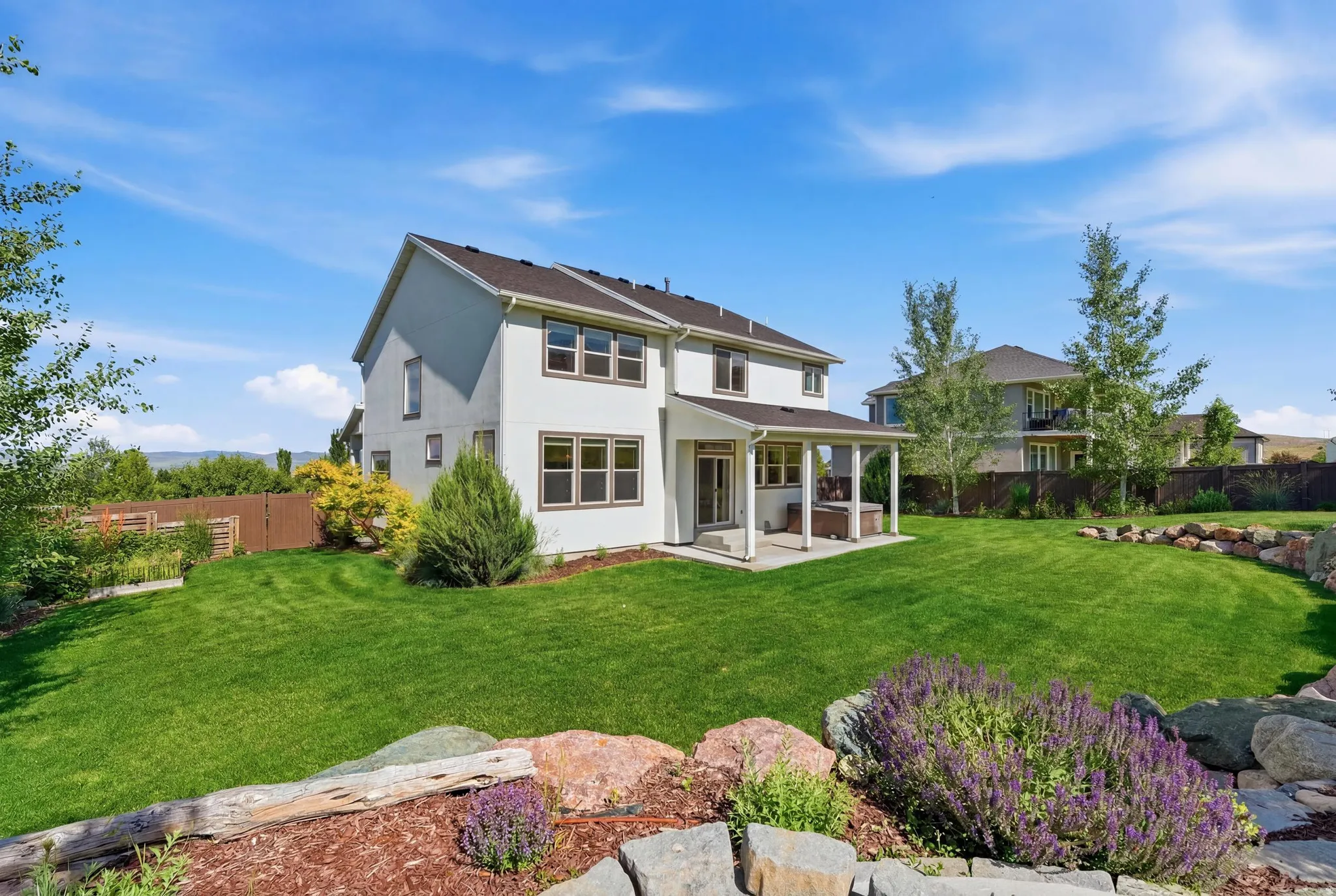 Expansive backyard with a covered patio, manicured lawn, and natural rock landscaping