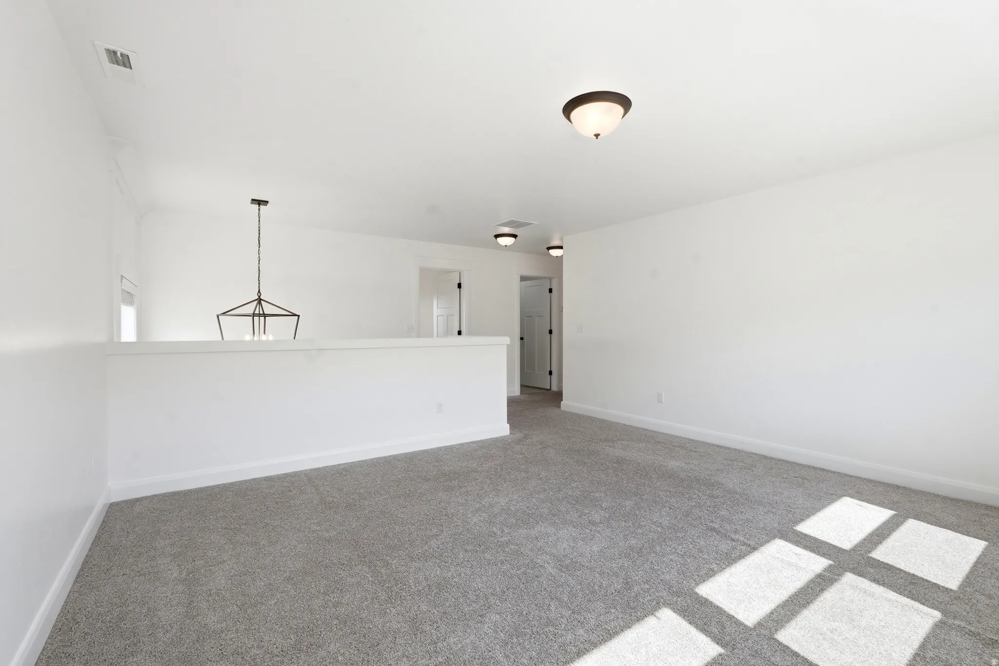 Spacious carpeted room featuring a partial wall, a geometric chandelier, and multiple doors