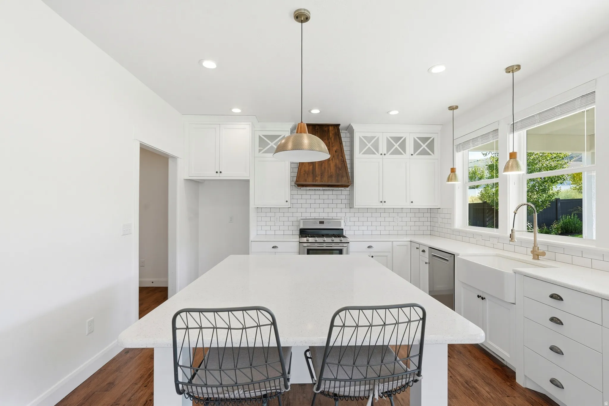 Kitchen featuring a large center island with a white countertop, white shaker cabinetry, white subway tile backsplash, and a wood-finish range hood