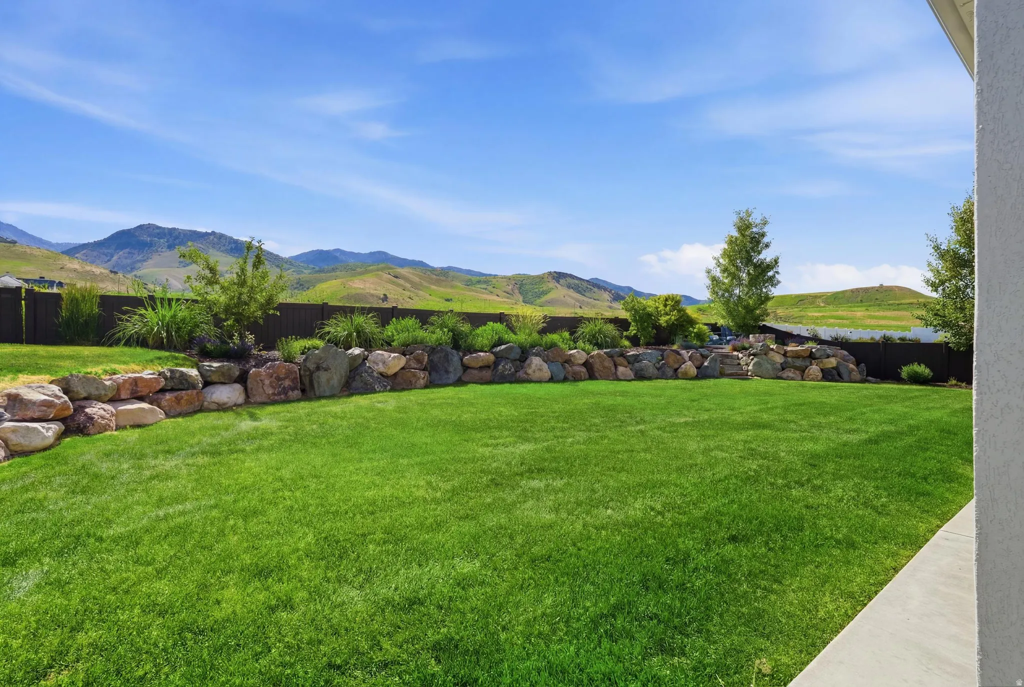 Expansive green lawn with a rock retaining wall and mature landscaping