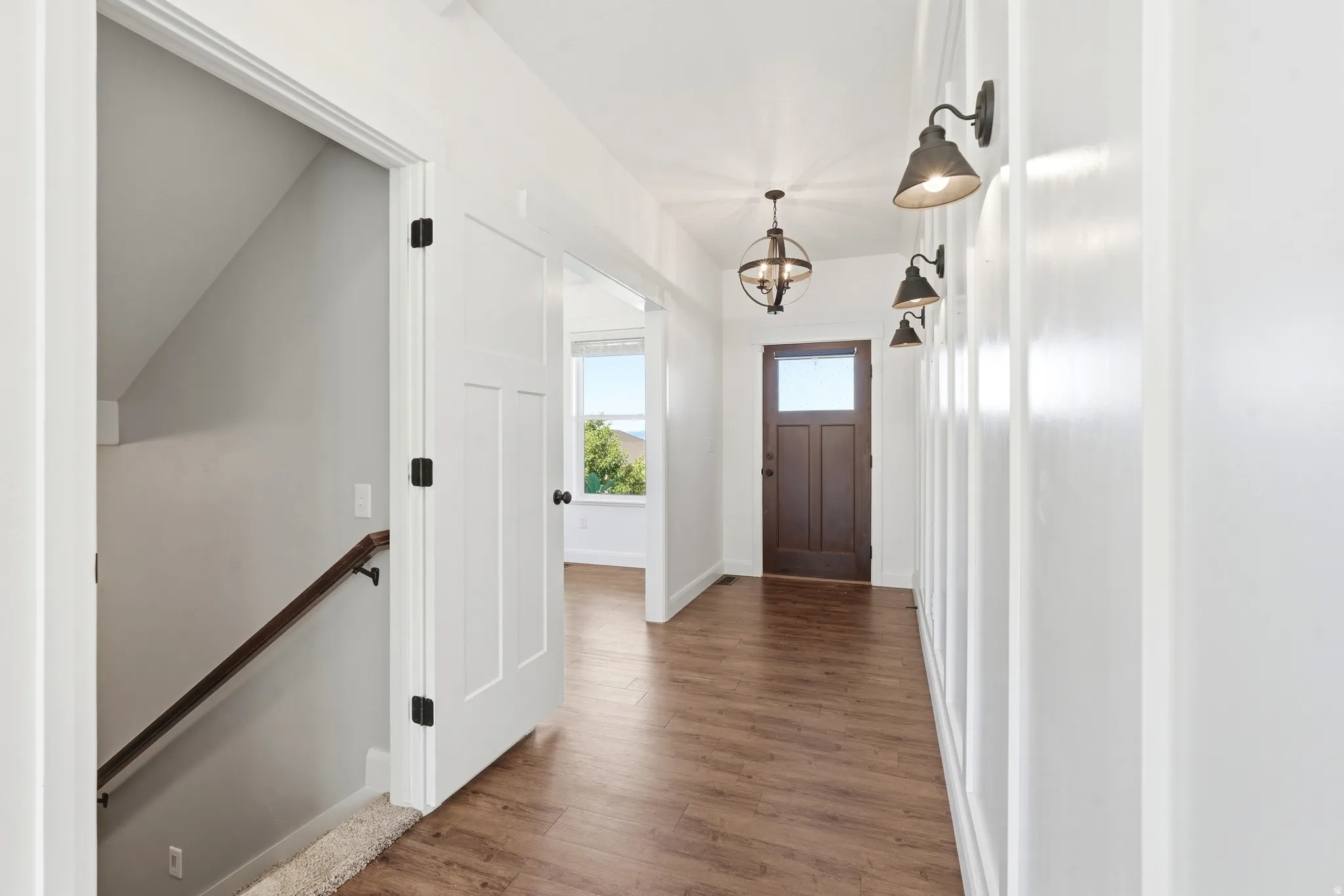Entryway featuring wood-finish flooring, a dark wood front door with glass panel, white paneled walls, and a contemporary chandelier