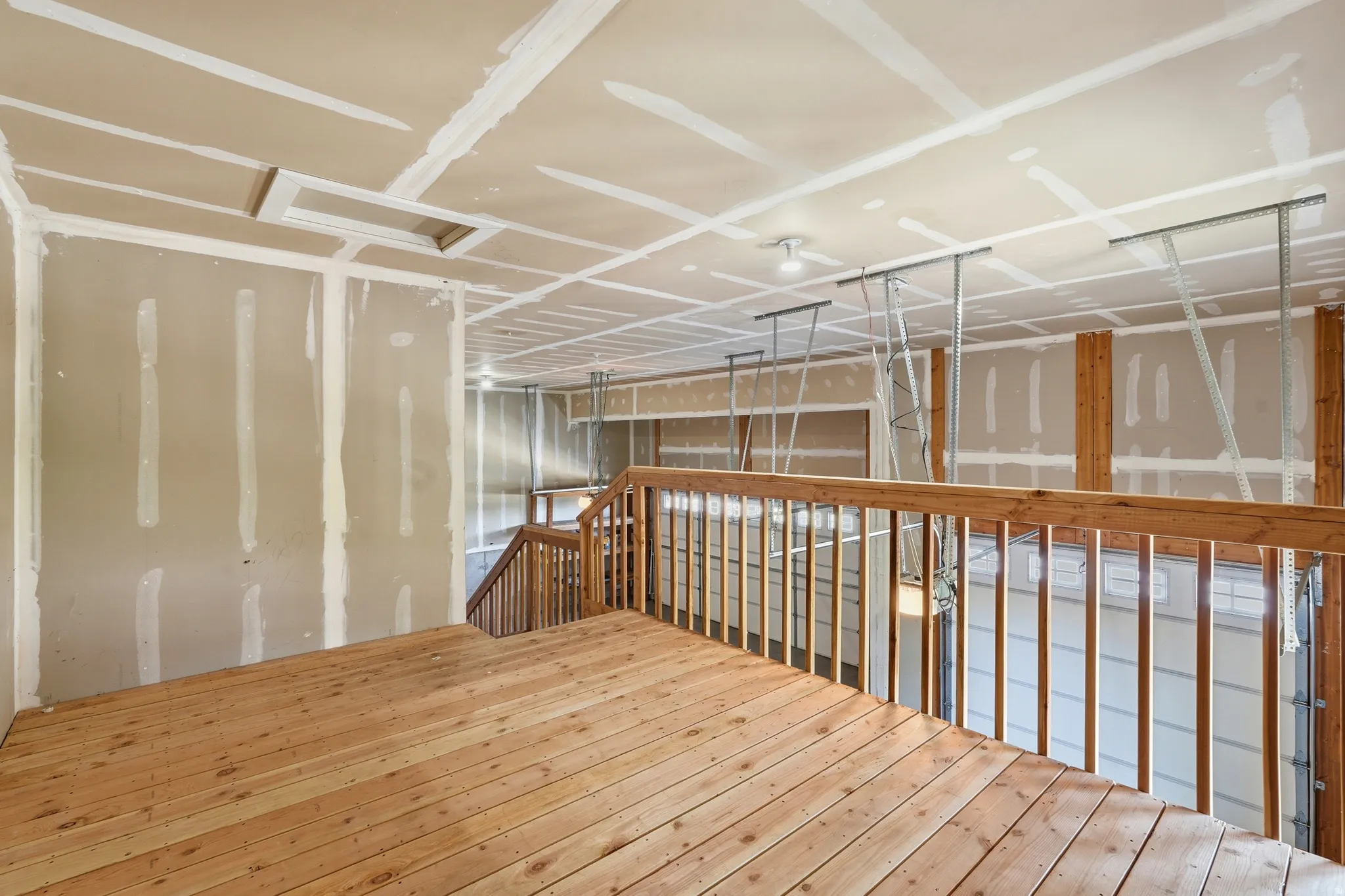 Unfinished interior space featuring a wood-finish floor, wood railing, drywall walls, and an unfinished ceiling