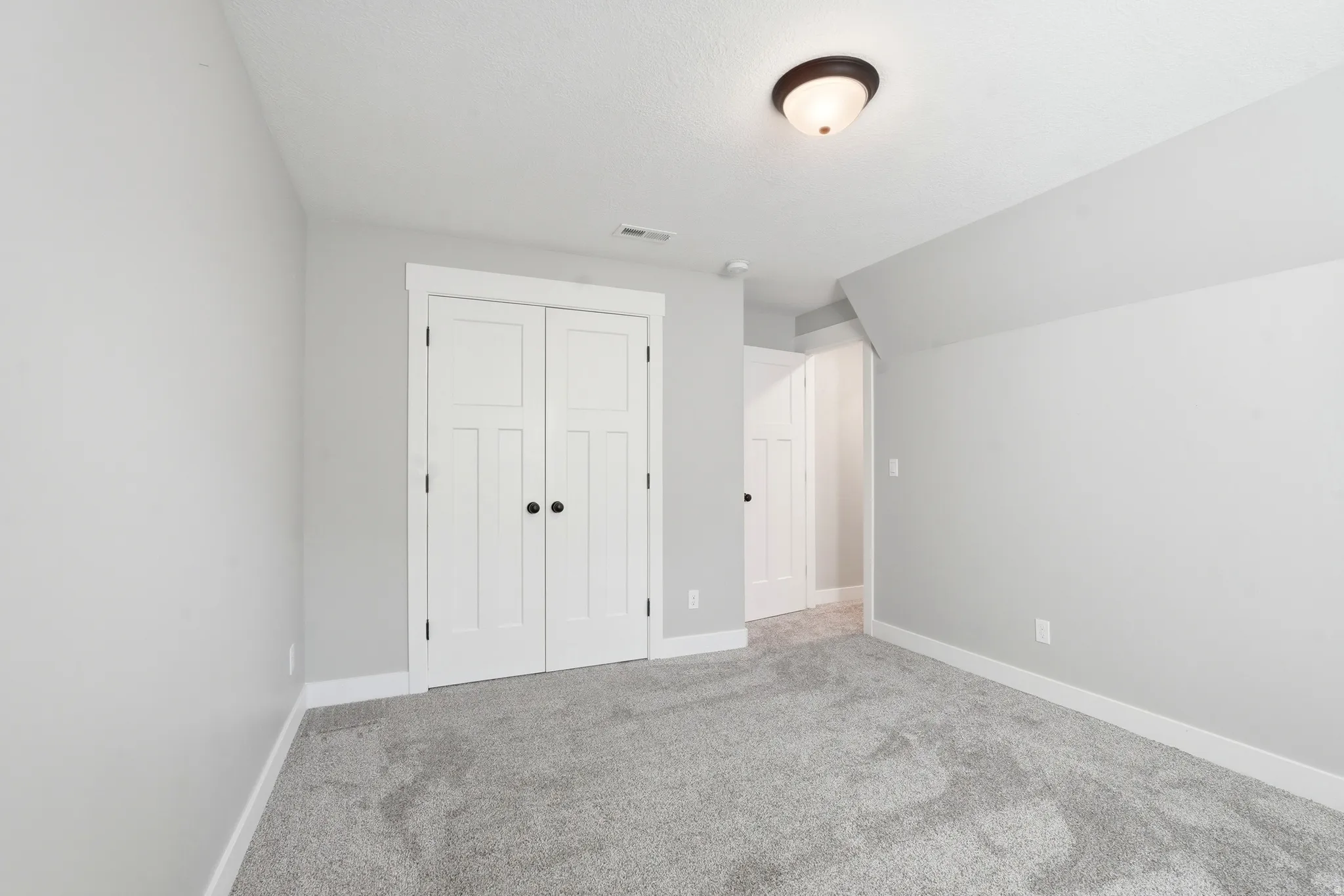 Spacious room featuring light gray wall paint, white trim, gray carpet flooring, a ceiling-mounted light fixture, and double white paneled doors