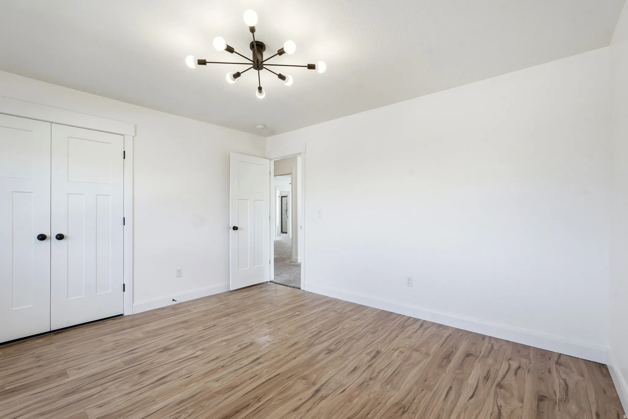 Room featuring wood-finish flooring, white walls, and a modern sputnik chandelier