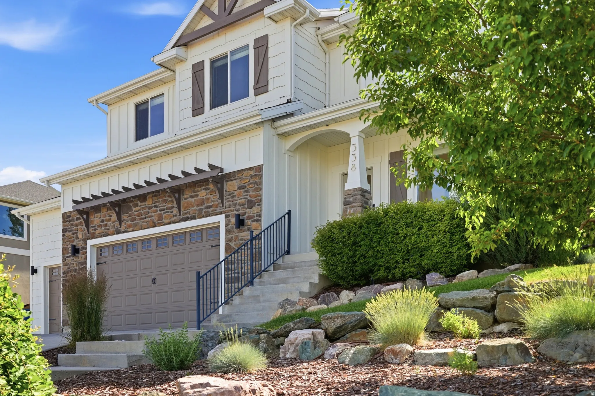 Two-story residence featuring light-colored siding, a stone facade, and dark brown window shutters