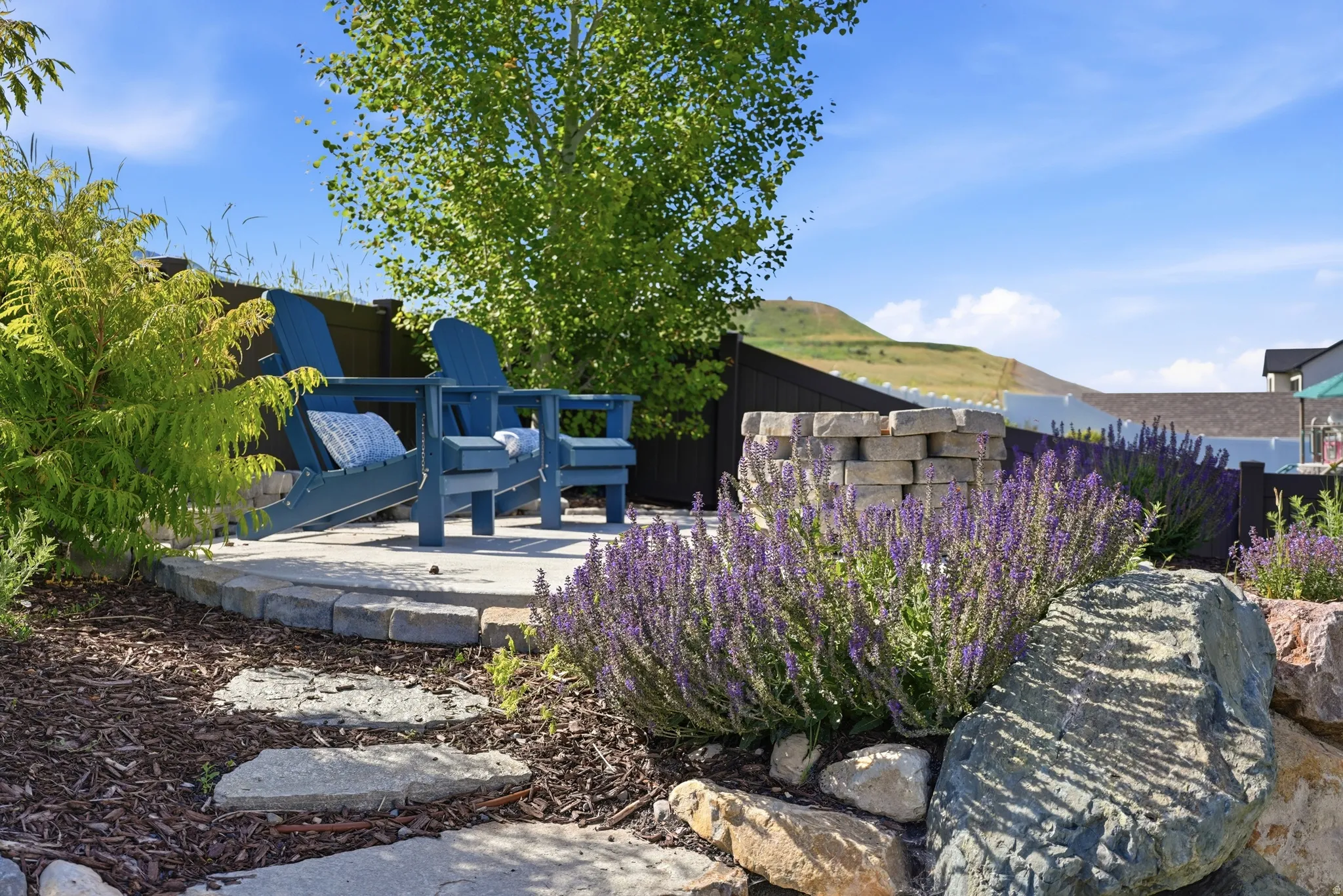 Landscaped backyard area featuring a stone-paved patio, a built-in stone fire pit, and mature plantings