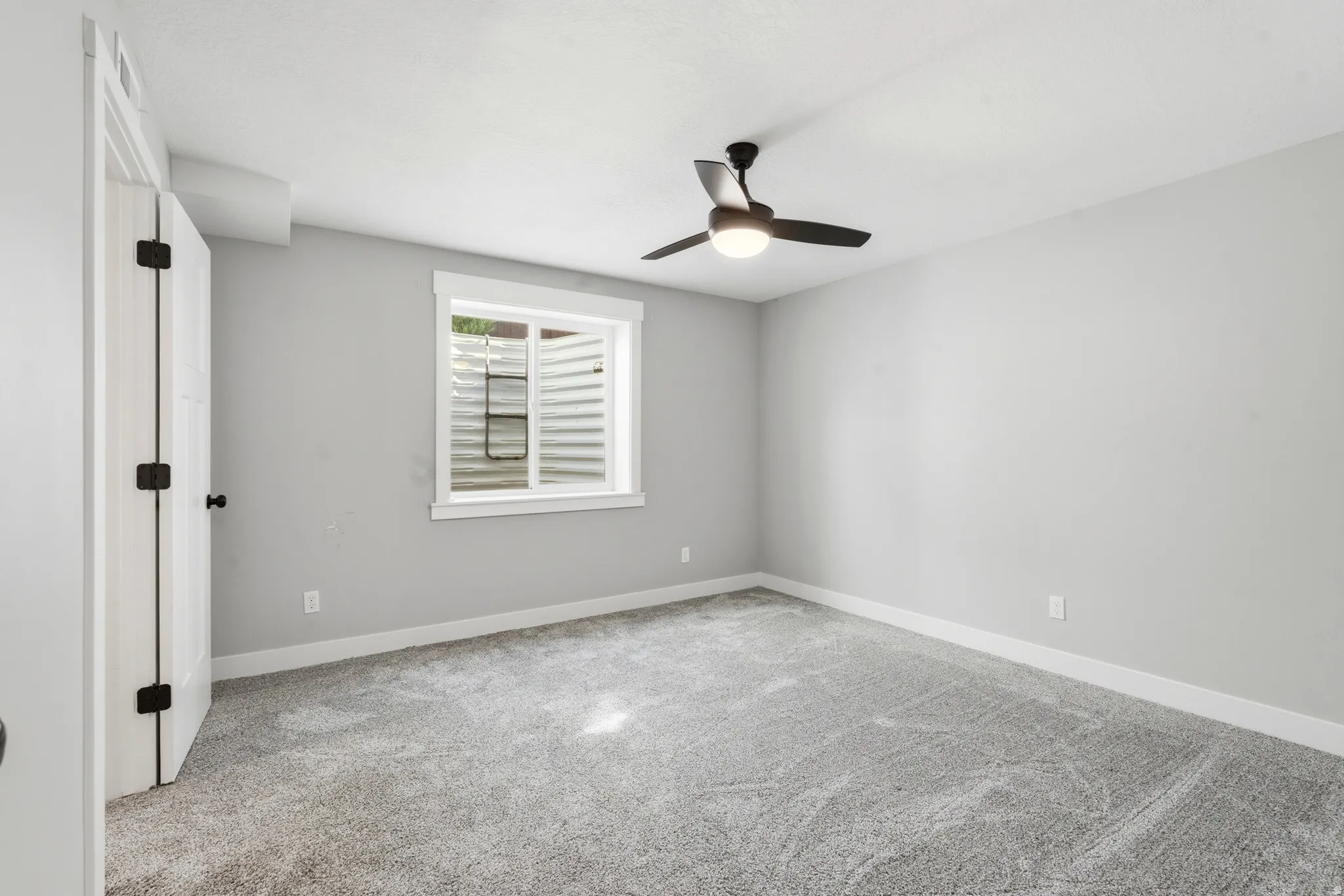 Room featuring gray carpeting, light gray walls, a white-framed window, and a black ceiling fan with integrated lighting