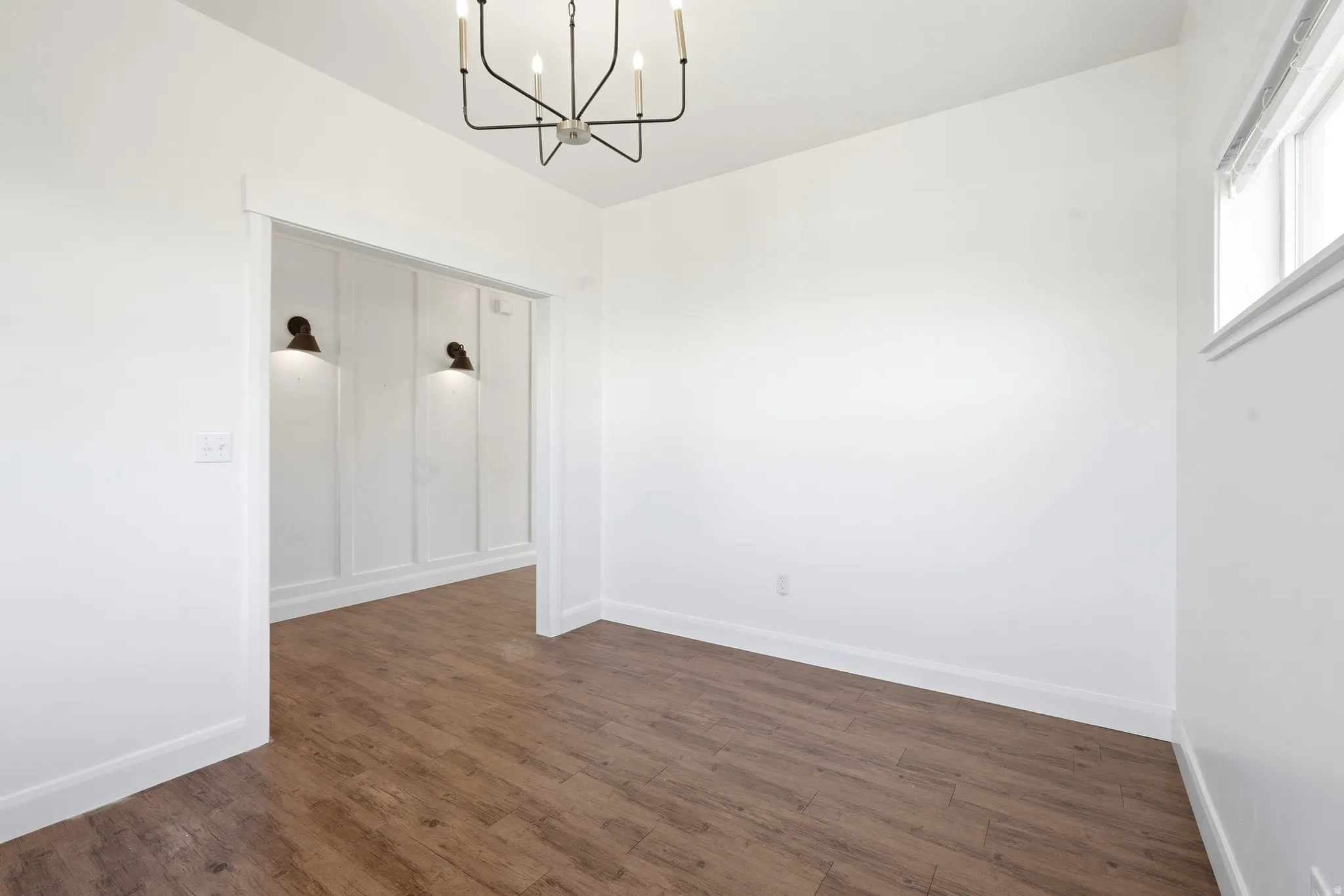 Expansive room featuring wood-finish flooring, a contemporary chandelier, and a window with white trim