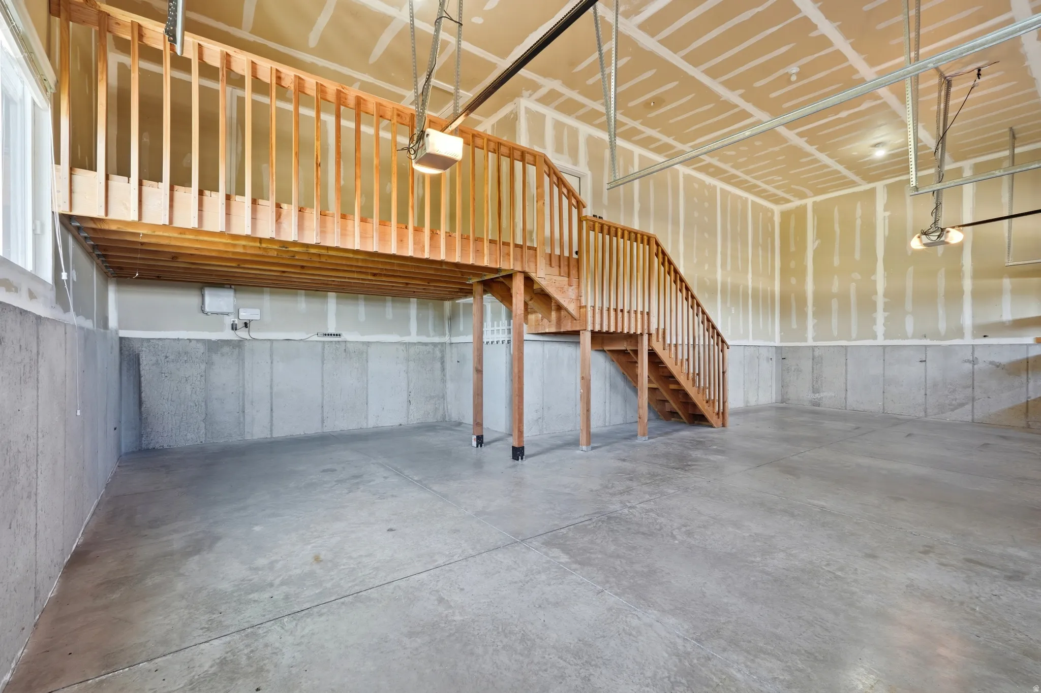 Spacious garage interior featuring concrete flooring and a wood staircase leading to an elevated storage area