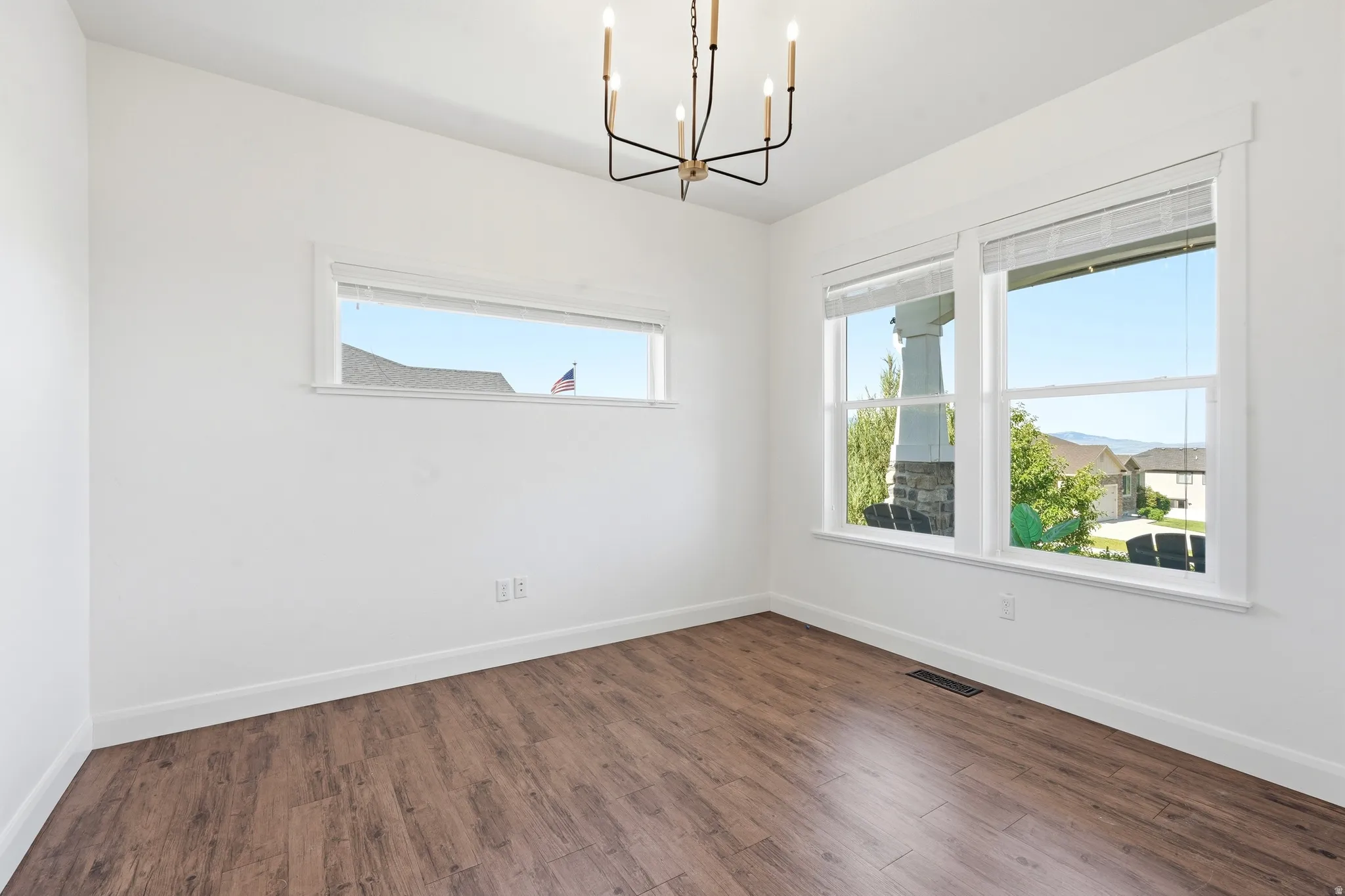 Spacious room featuring wood-finish flooring, white baseboards, and white walls