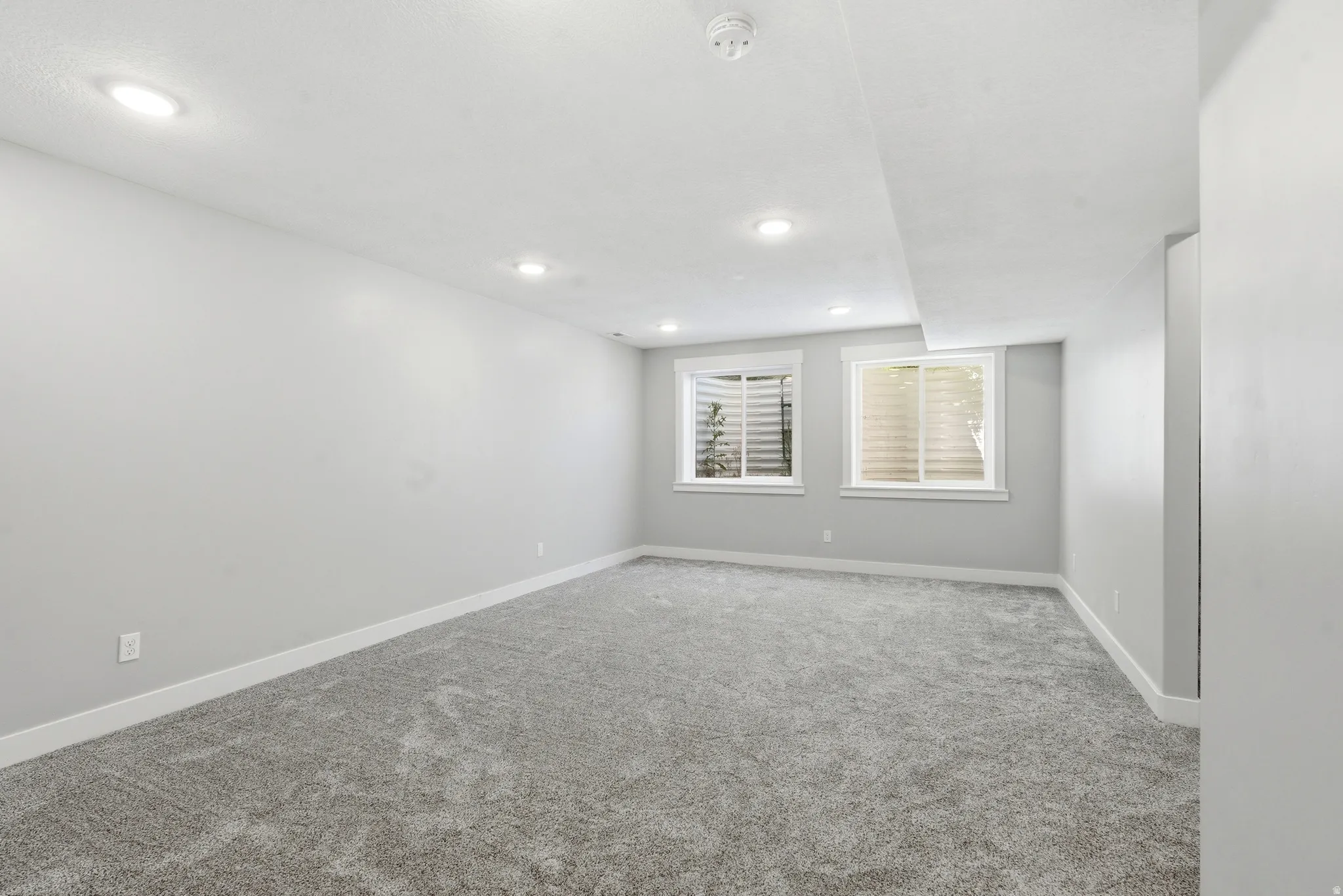 Spacious room featuring neutral gray walls, gray carpeting, and recessed lighting