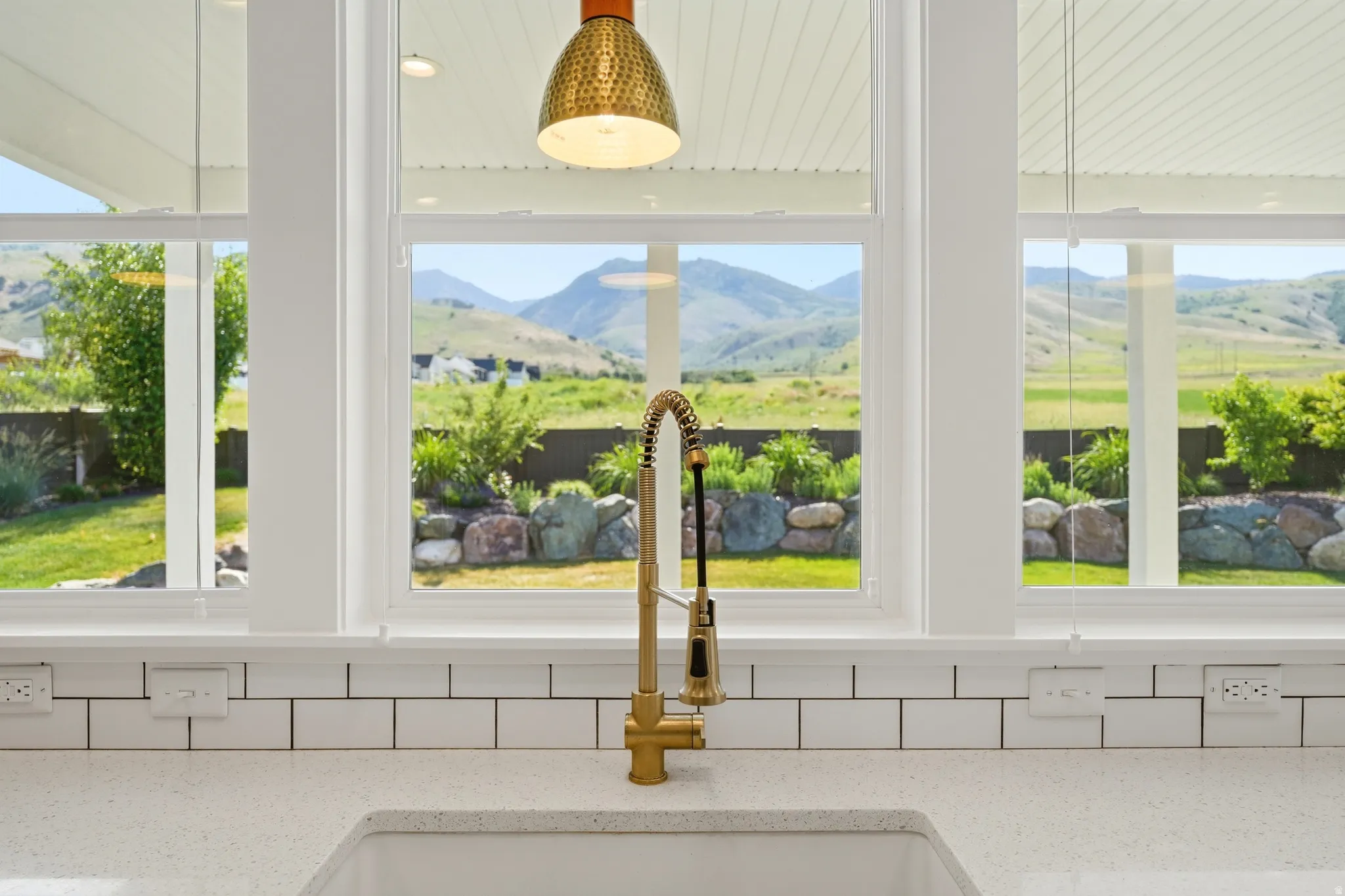 Kitchen sink area featuring a gold-tone faucet, white subway tile backsplash, and light-toned countertop
