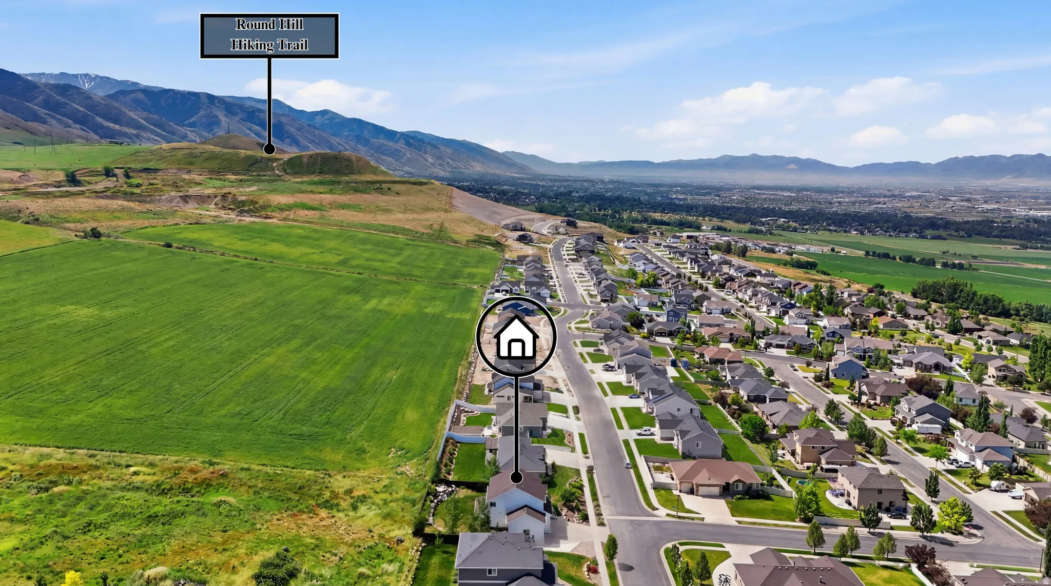 Aerial perspective showcasing a residential development alongside expansive green fields and distant mountains