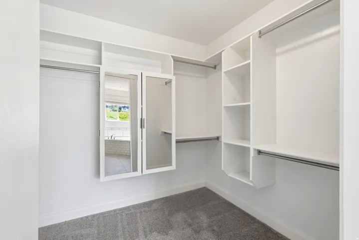 Walk-in closet featuring white built-in shelving, multiple hanging rods, and a mirrored cabinet