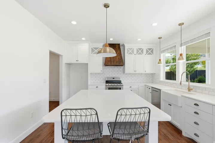 Kitchen featuring a large center island with a white countertop, white shaker cabinetry, white subway tile backsplash, and a wood-finish range hood