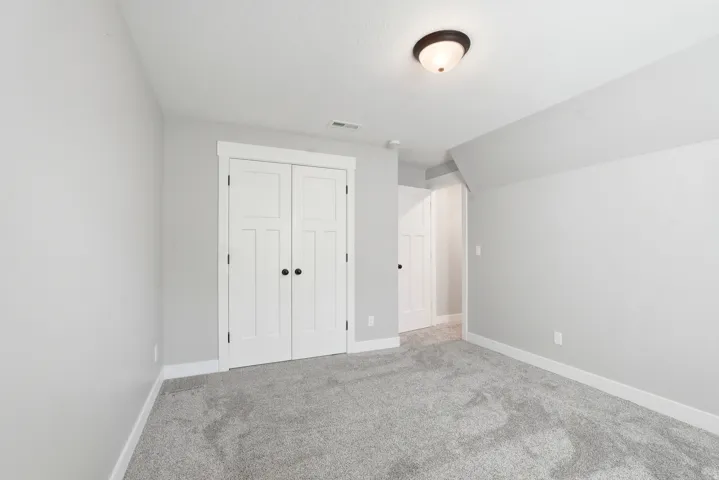 Spacious room featuring light gray wall paint, white trim, gray carpet flooring, a ceiling-mounted light fixture, and double white paneled doors