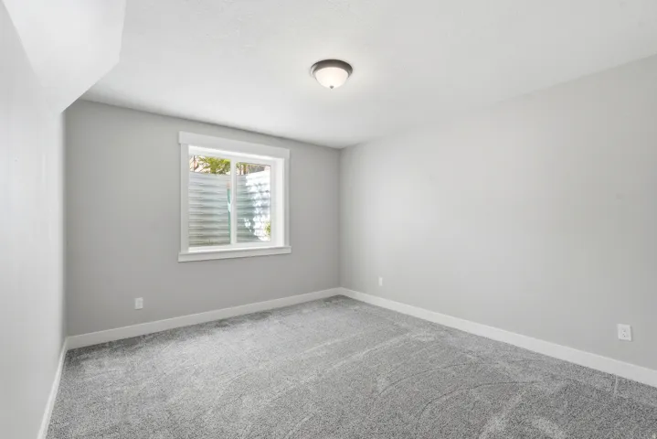 Bedroom featuring light gray walls, plush gray carpeting, a single window with white trim, and a ceiling-mounted light fixture