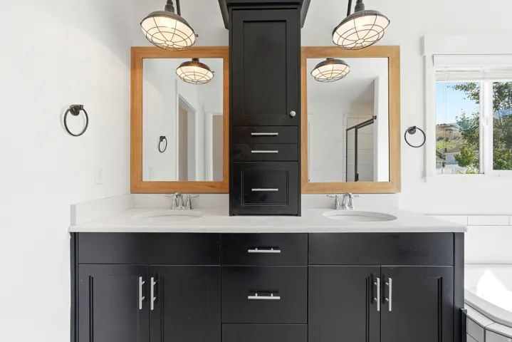 Double vanity featuring black cabinetry, light-toned countertops, dual undermount sinks, and two wooden-framed mirrors
