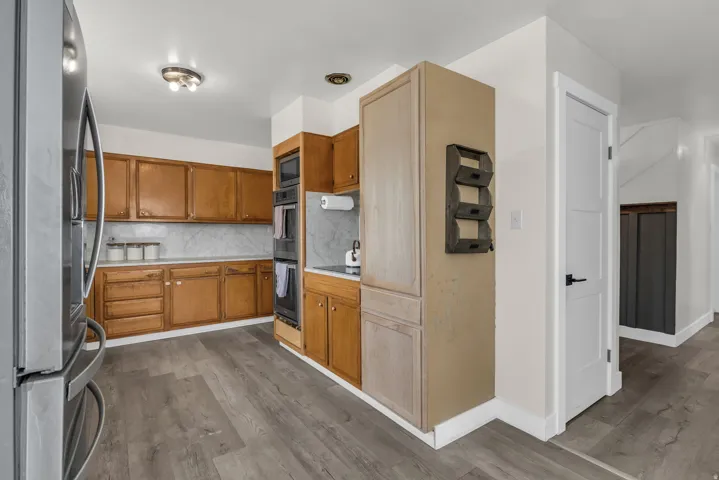 Kitchen featuring wood cabinetry, stainless steel refrigerator, built-in double ovens, and wood-finish flooring