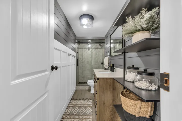 Contemporary bathroom featuring a wood-finish vanity with a light-colored countertop, matte black fixtures, and a rectangular mirror