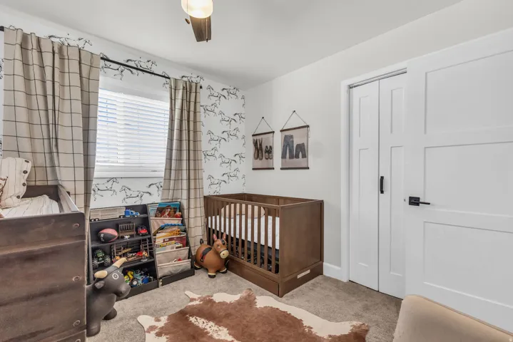 Interior room featuring neutral wall paint, patterned accent wall, light brown carpeting, and a window with blinds and grid-patterned drapes
