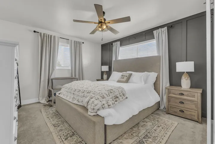 Bedroom featuring a dark accent wall with paneling, light gray carpeting, and a ceiling fan with integrated lighting