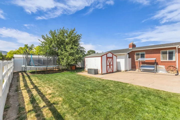 Expansive backyard featuring a manicured lawn, a white fence, a red brick exterior, a paved patio, and a storage shed