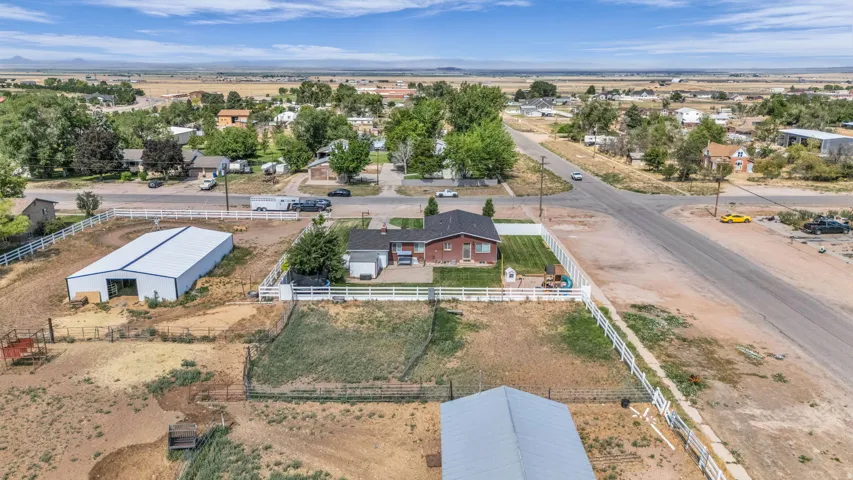Expansive property featuring a brick ranch-style residence, a large metal outbuilding, a white vinyl fence enclosing a manicured lawn, and multiple sections of open land