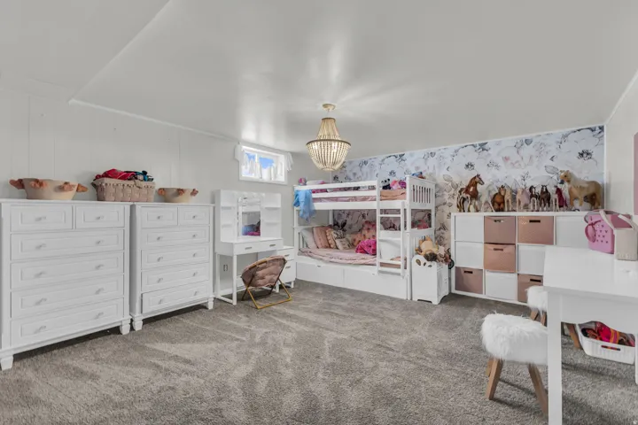 Spacious room featuring light gray carpeting, crisp white walls, a single window, and an overhead chandelier light fixture